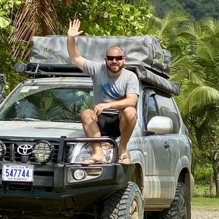 Johannes Leuschner sitzt winkend auf der Motorhaube eines Geländewagens mit Dachzelt.